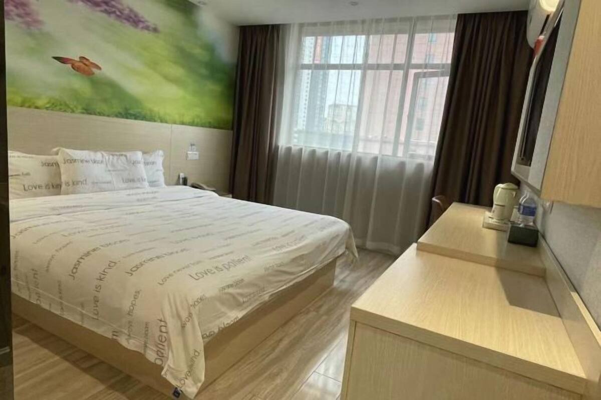 A hotel room with a bed, a desk, a window with curtains, and a wall with a nature-themed mural.
