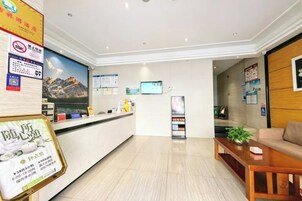 Uma área de recepção de hotel, com balcão de atendimento, tela de televisão e espaço de estar com sofá e mesa de centro.