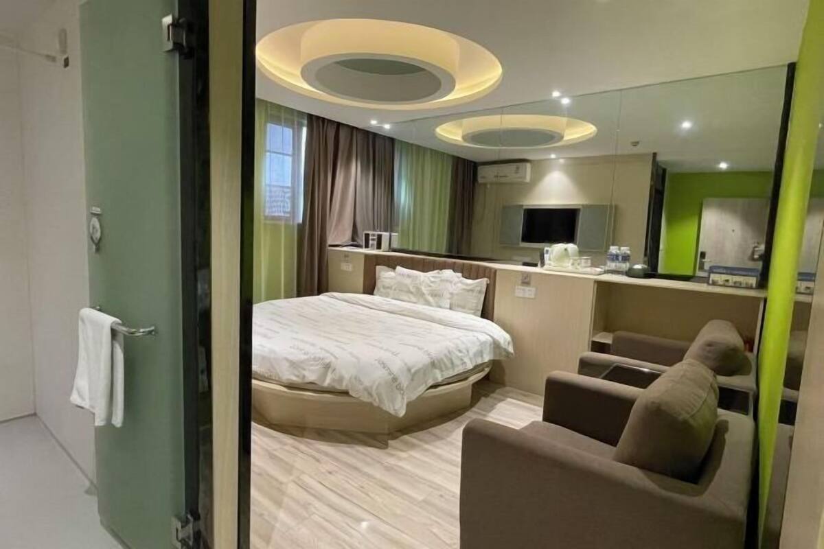 A hotel room with a bed, a sitting area, a mirror, and a television.