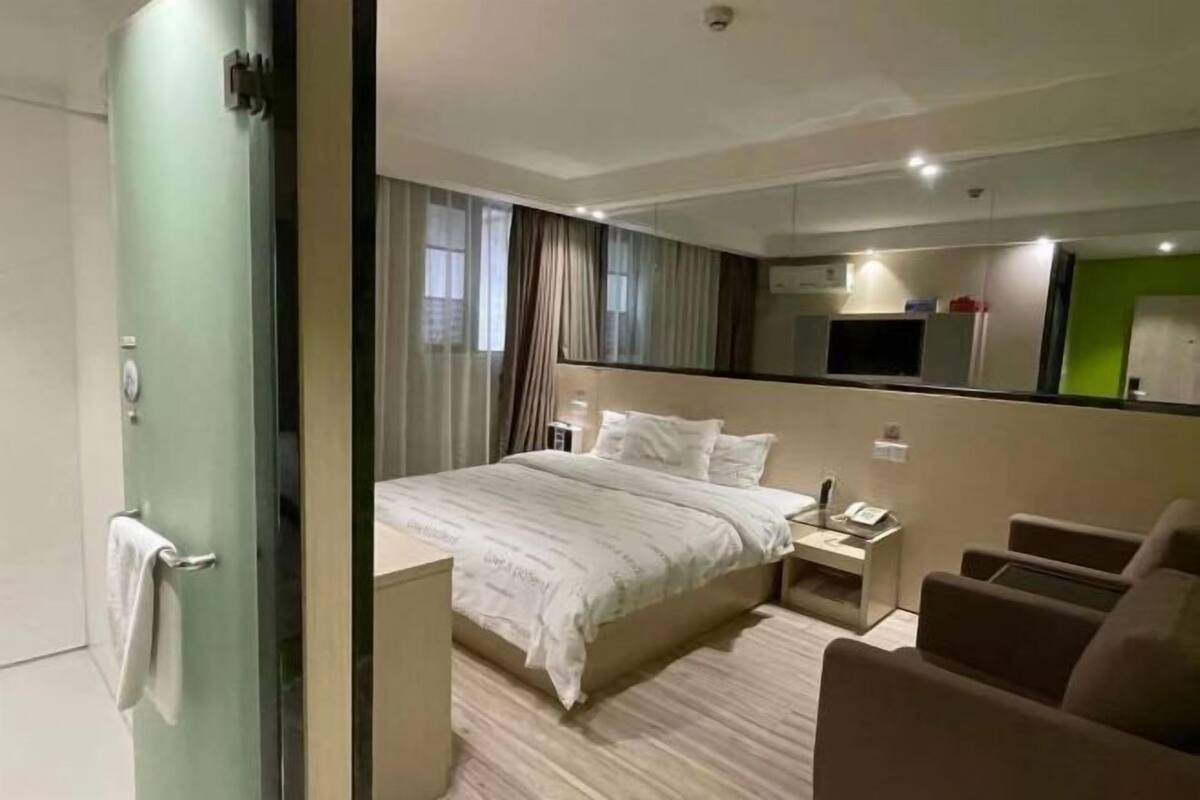 A modern hotel room with a bed, a desk, a chair, and a mirror.