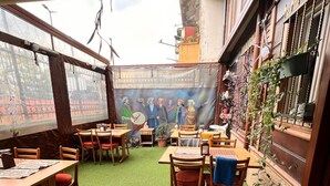 An outdoor dining area with tables and chairs, a mural on the wall, and a view of the street. - April Story Apart Hotel (Istanbul)