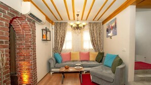 A living room with a brick fireplace, a grey sofa with colorful cushions, a wooden coffee table, and a chandelier. - April Story Apart Hotel (Istanbul)