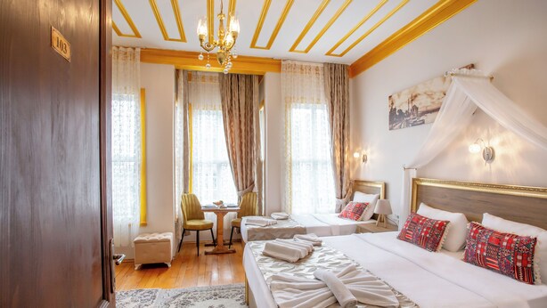 A hotel room with a large bed, two bedside tables, a desk with a chair, a small ottoman, and a chandelier. - April Story Apart Hotel (Istanbul)