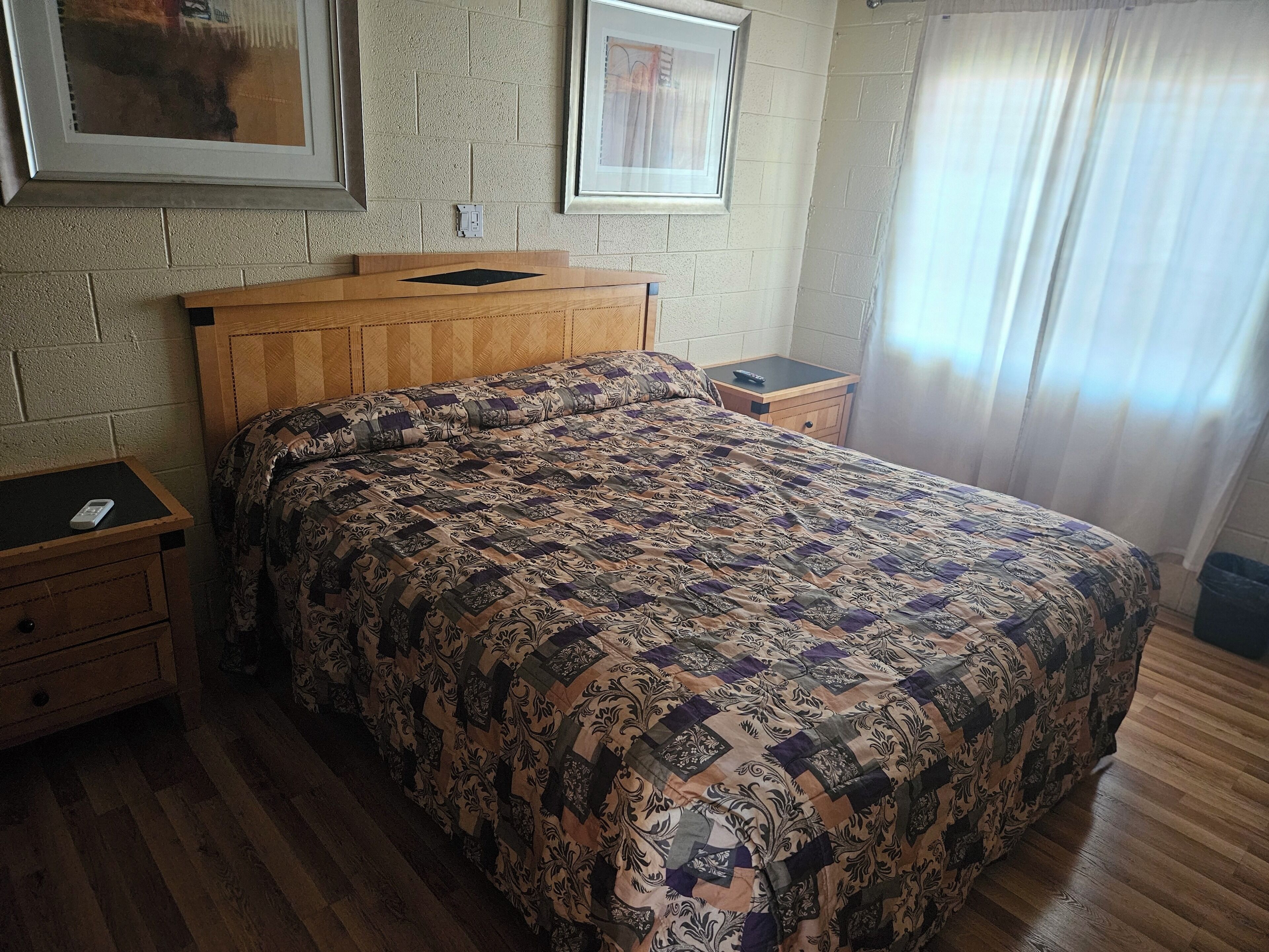 Una cama bien hecha con una colcha estampada, un cabecero de madera y dos mesitas de noche, una de ellas con un control remoto.