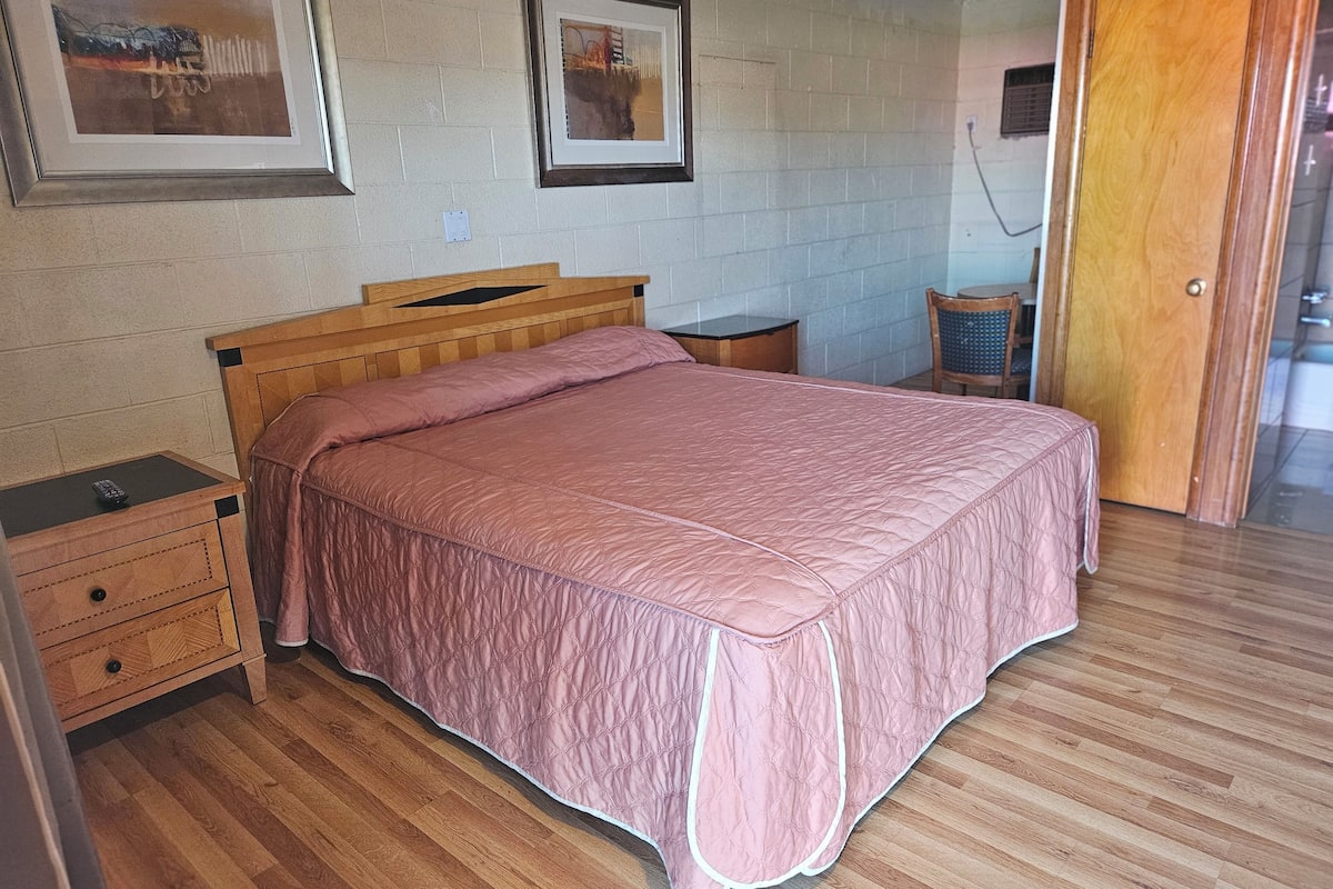 Un dormitorio con una cama de madera, una mesita de noche, una silla y una puerta.