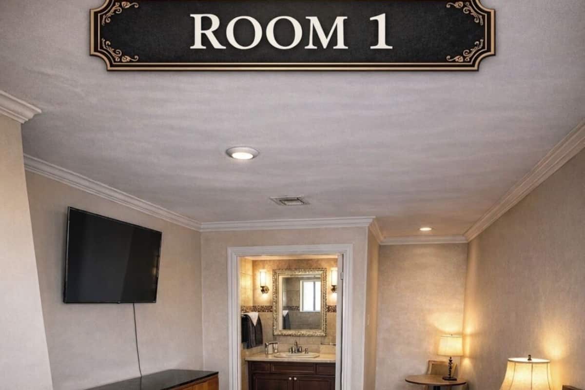 Habitación de hotel con cama, televisión, cómoda, tocador con espejo y una pequeña mesa con lámpara.
