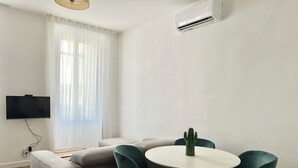 Een moderne woonkamer met een grijze bank, smaragdgroene stoelen, een witte tafel en een cactus als middelpunt.