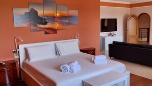 A hotel room with a large bed, a sofa, a TV, and artwork on the wall. - Villa Giulia (Syracuse)