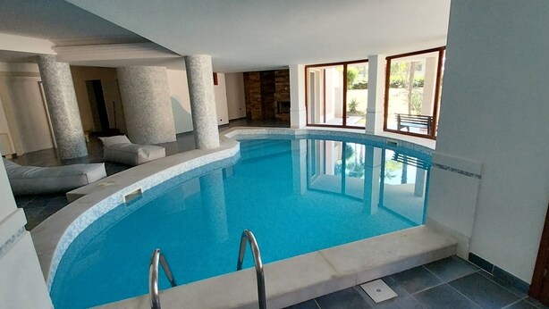 An indoor swimming pool with clear blue water, surrounded by white walls and columns, and large windows allowing natural light. - Villa Giulia (Syracuse)