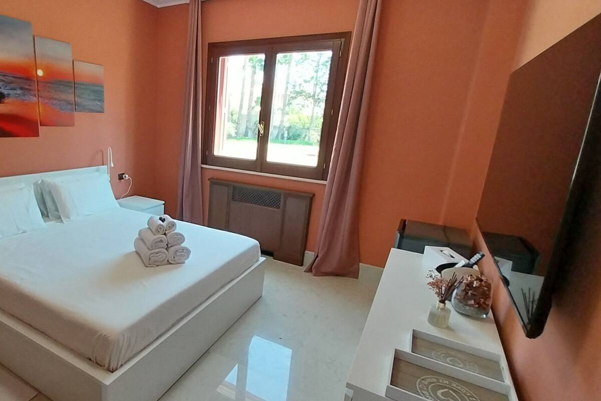 A bedroom with a bed, bedside tables, a TV, and a window with curtains.