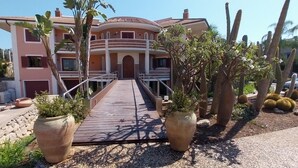 A multi-story house with a wooden deck leading to a gated entrance, surrounded by cacti and potted plants. - Villa Giulia (Syracuse)