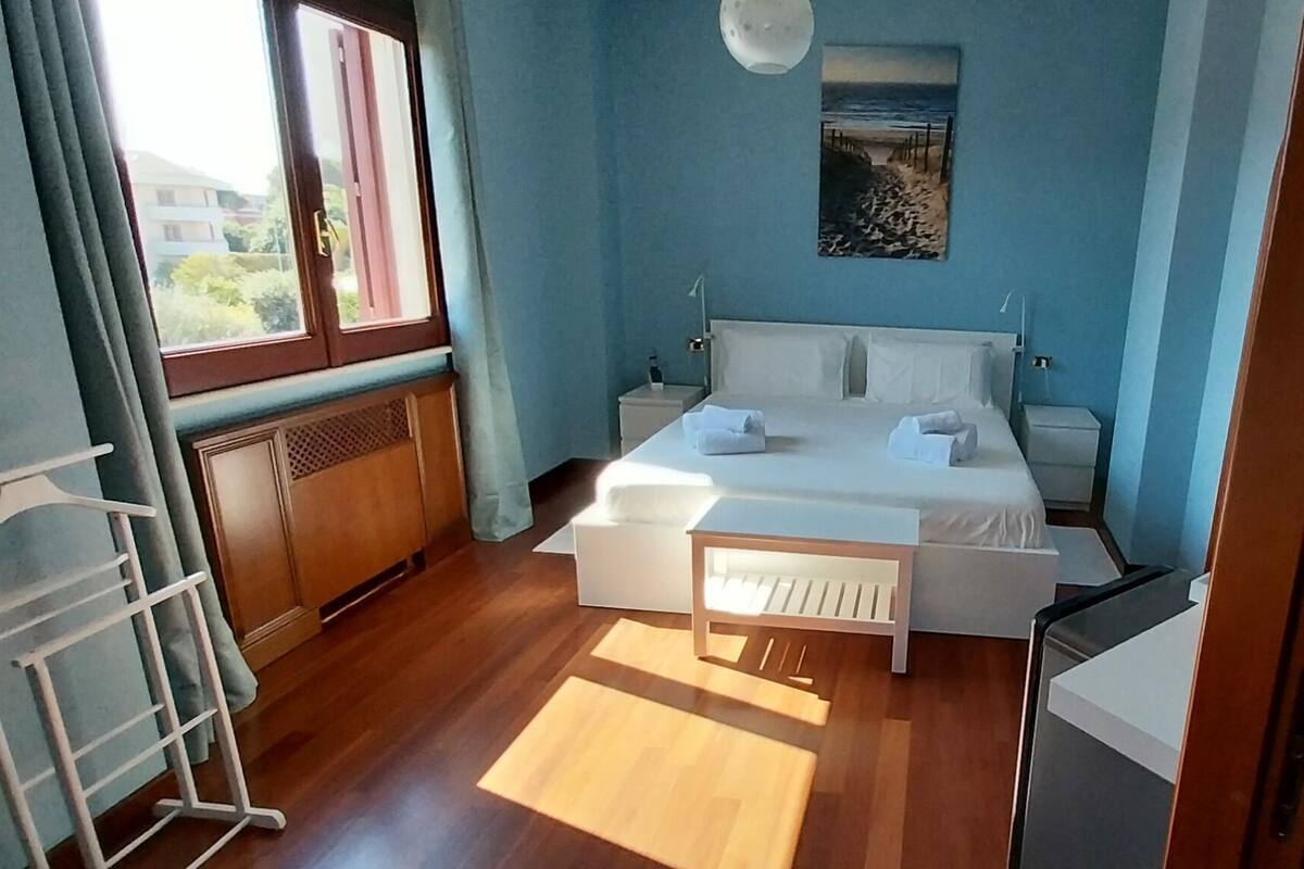 A bedroom with a bed, bedside tables, a window, and a painting on the wall.