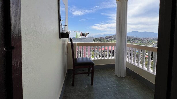 Un balcón con una silla, un espejo colgante y vistas a una ciudad y montañas.
