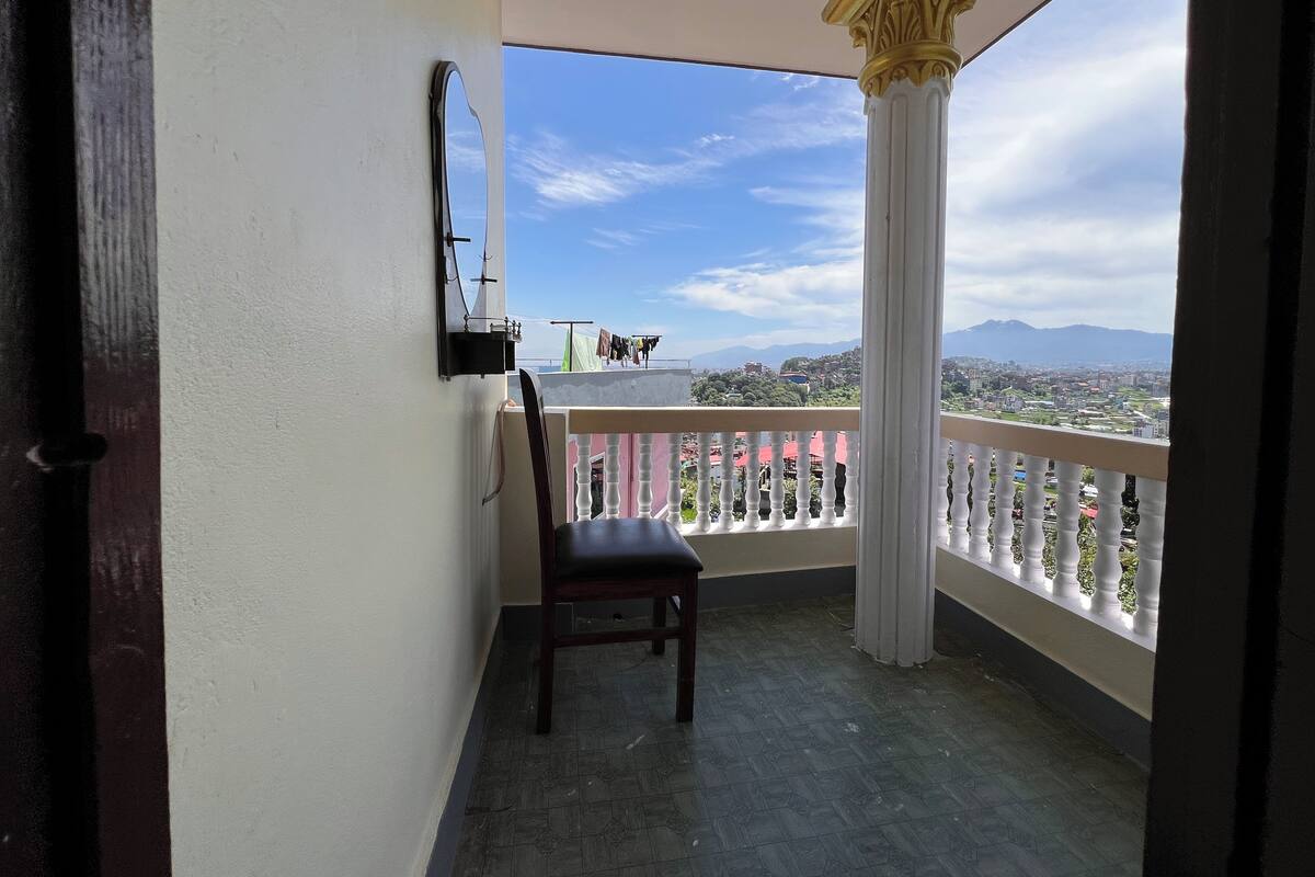 A balcony with a chair, a hanging mirror, and a view of a cityscape and mountains.