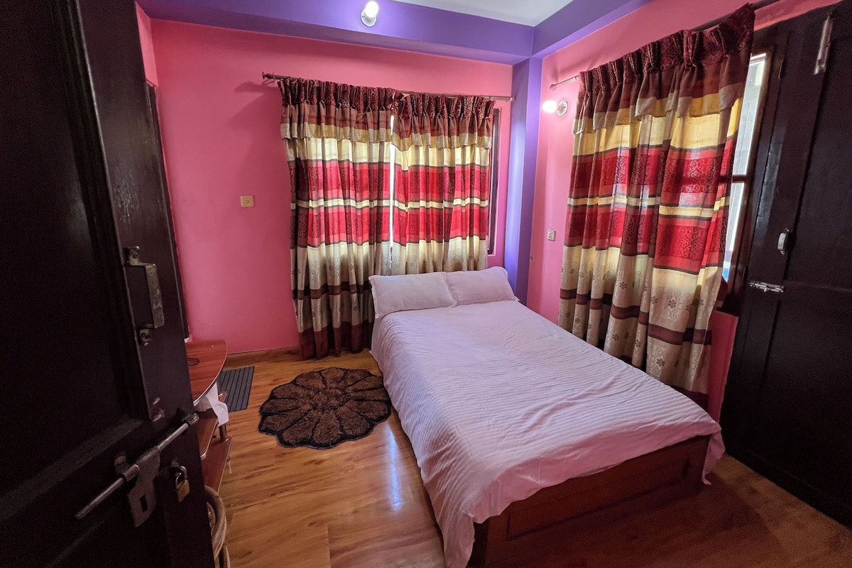 A bedroom with a bed, curtains, a wooden floor, and a door.