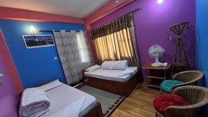 Una habitación con dos camas, un escritorio, una silla, un ventilador de pie y una ventana con cortinas.