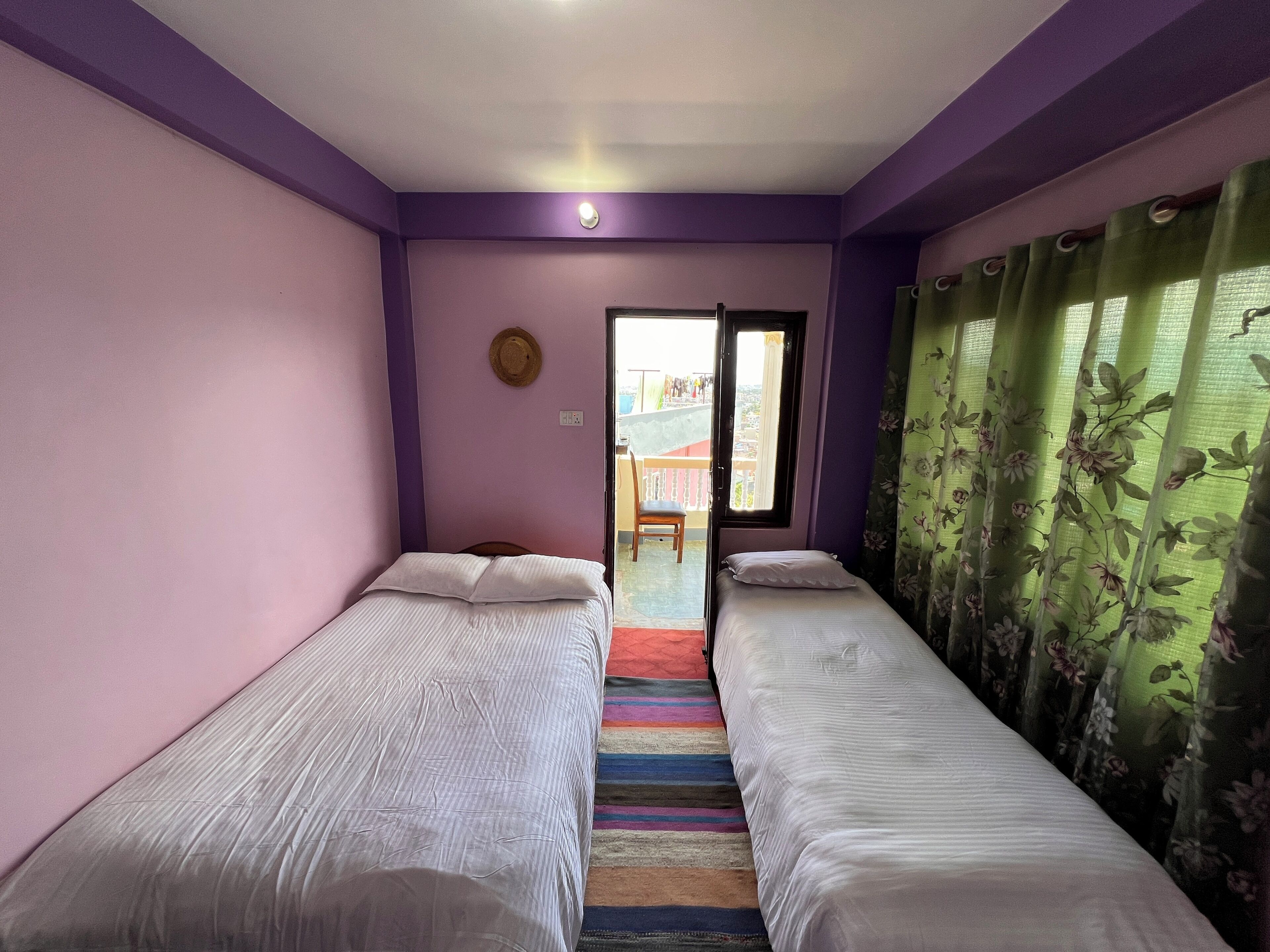 Une chambre avec deux lits simples, une fenêtre avec des rideaux et une porte donnant sur l’extérieur.