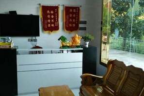 A reception area with a desk, two red banners, a television, and a window with a view of trees. - Hengyang Nanyueshan Xiangyuan Manor (Hengyang)