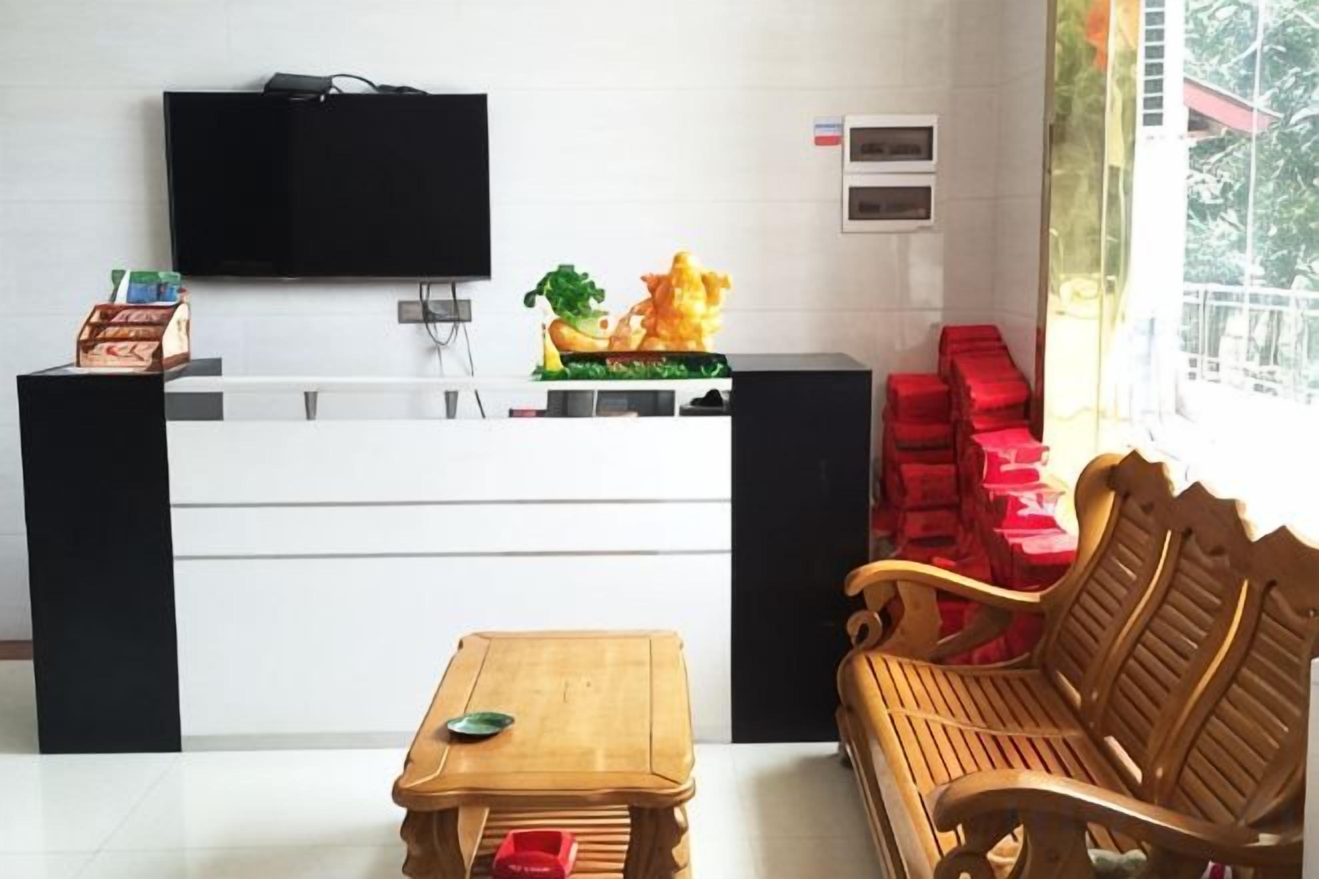 A reception area with a flat-screen TV, a wooden bench, a small table, and a window with red boxes outside.