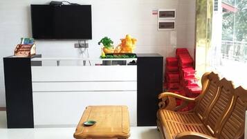 A reception area with a flat-screen TV, a wooden bench, a small table, and a window with red boxes outside.