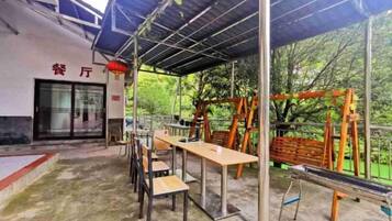 An outdoor seating area with tables and chairs, a covered shelter, and a playground with swings and climbing structures.