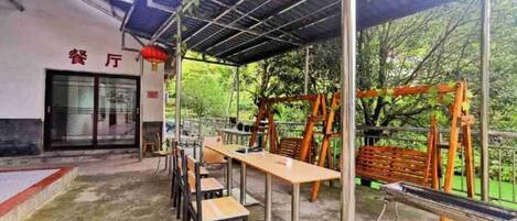 An outdoor seating area with tables and chairs, a covered shelter, and a playground with swings and climbing structures.