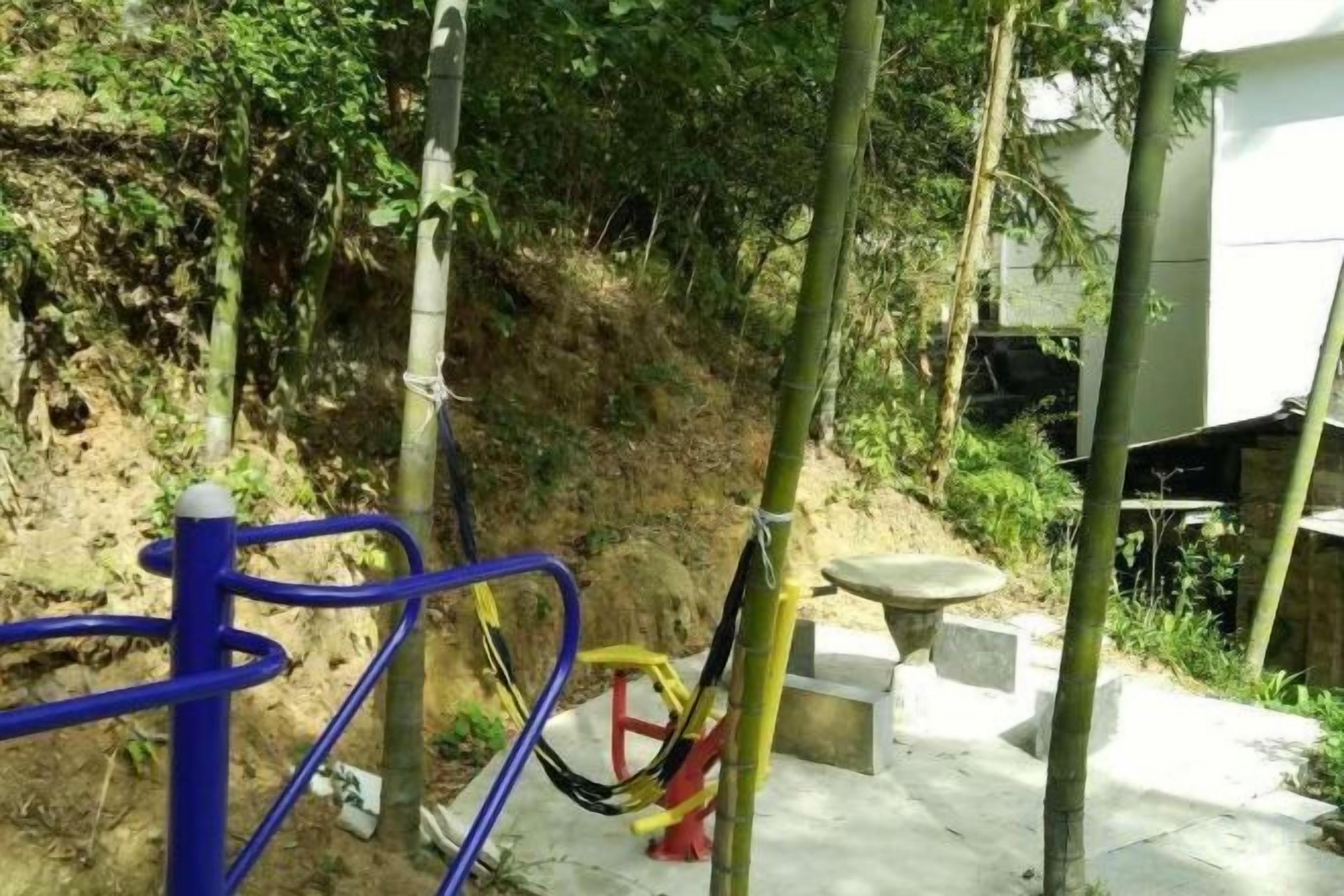 An outdoor area with exercise equipment, a concrete path, and a hillside.