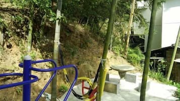 An outdoor area with exercise equipment, a concrete path, and a hillside.