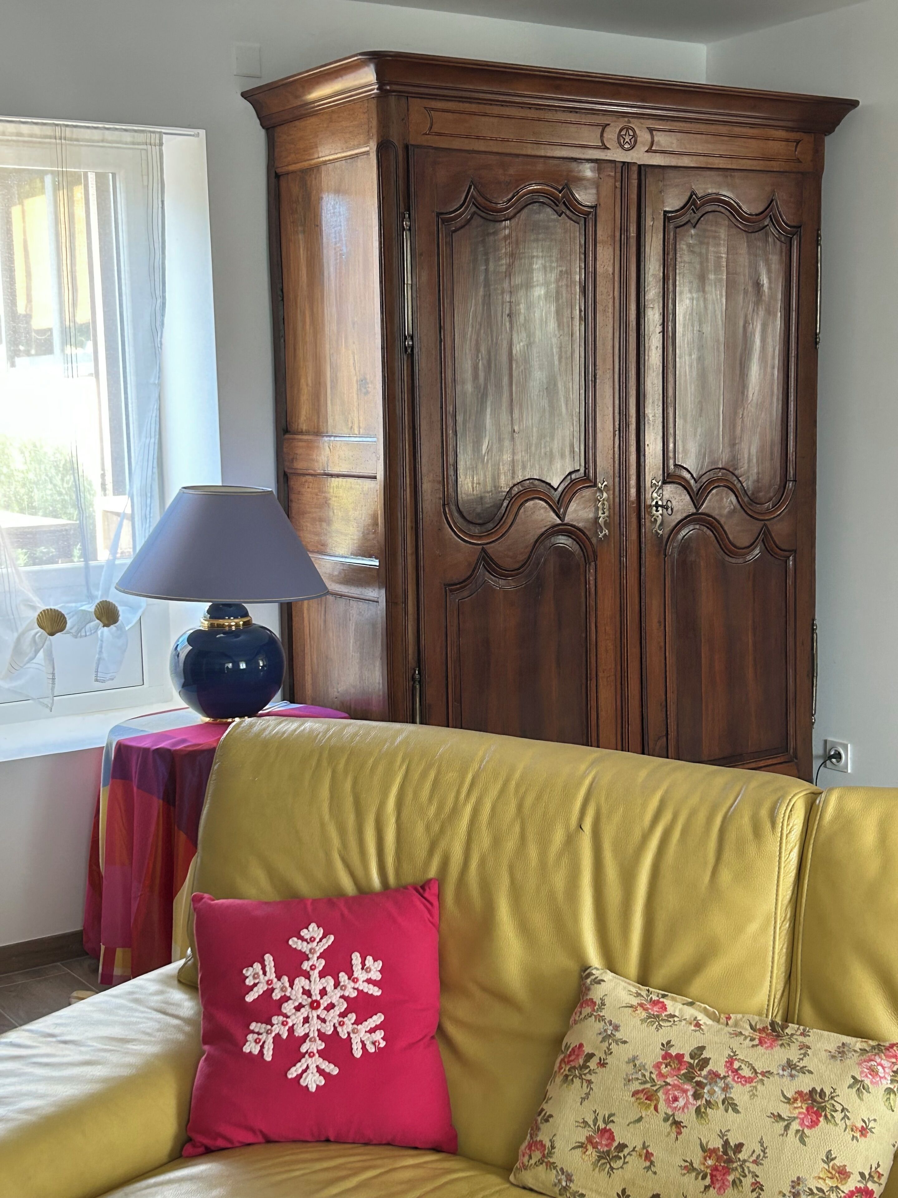 Habitació amb un sofà groc, un armari de fusta, una taula amb una làmpada i una finestra amb cortines.