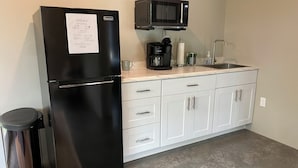 A compact kitchen with a black refrigerator, a microwave, a coffee maker, and a trash bin. - Cozy cottage in charming downtown Mount Vernon. (Mount Vernon)
