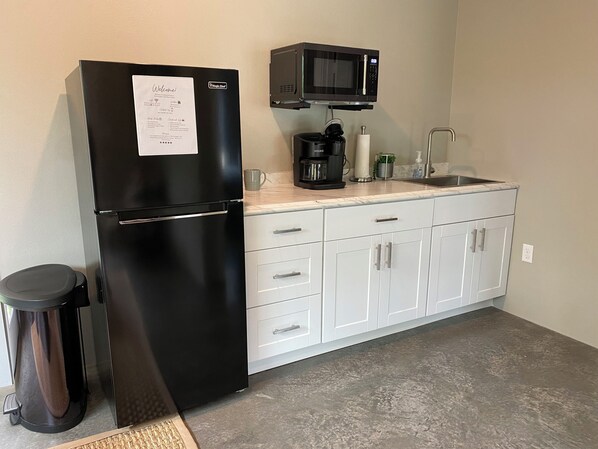 A compact kitchen with a black refrigerator, a microwave, a coffee maker, and a trash bin.