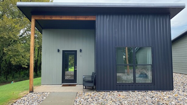 A modern building with a dark exterior, a wooden porch, a door, and a large window. - Cozy cottage in charming downtown Mount Vernon. (Mount Vernon)