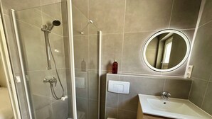 Un baño moderno con ducha de vidrio, inodoro y lavamanos con tocador de madera.