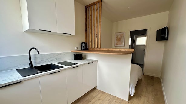 Una cocina compacta con armarios blancos, un lavamanos negro y una encimera de madera.