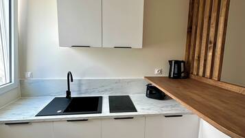 A compact kitchen with white cabinets, a black sink, a wooden countertop, and a coffee maker.