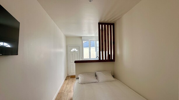 A bedroom with a bed, a window with vertical blinds, a door, and a mounted TV.