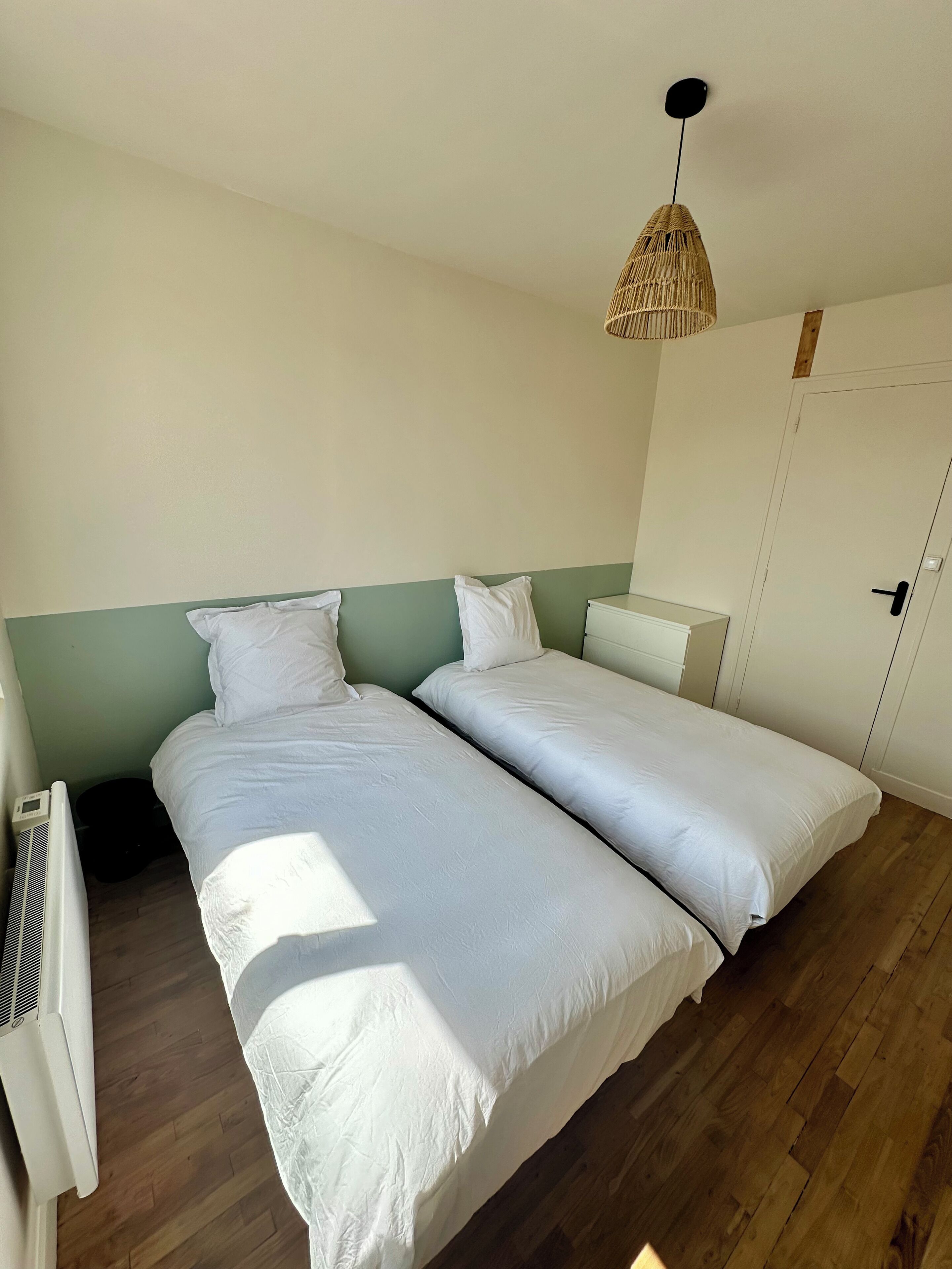 A bedroom with two beds, a ceiling fan, a wall-mounted heater, and a door.