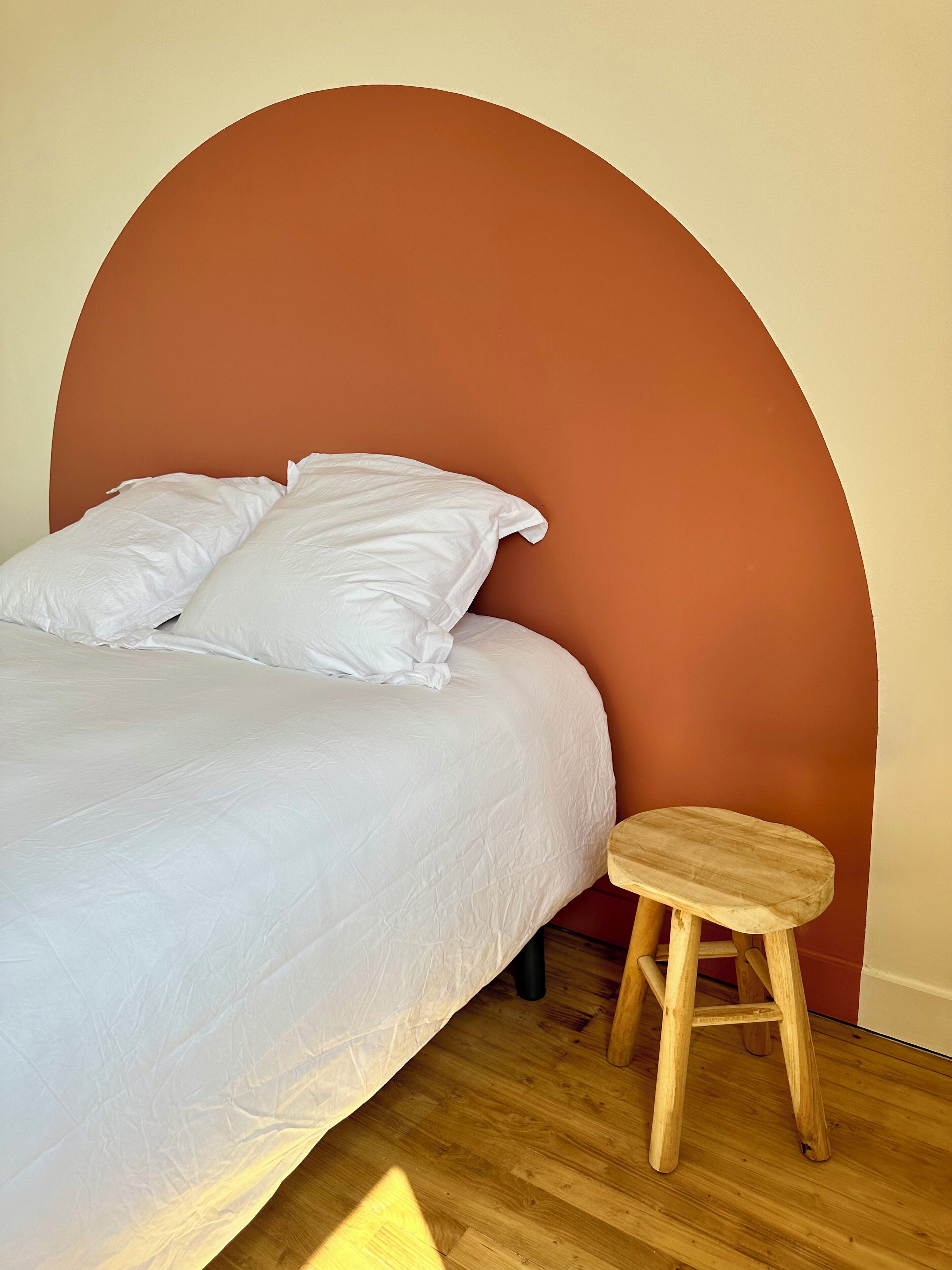 A bed with white bedding, a wooden stool, and a curved wall.