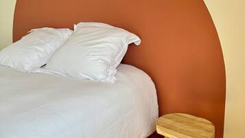A bed with white bedding, a wooden stool, and a curved wall.