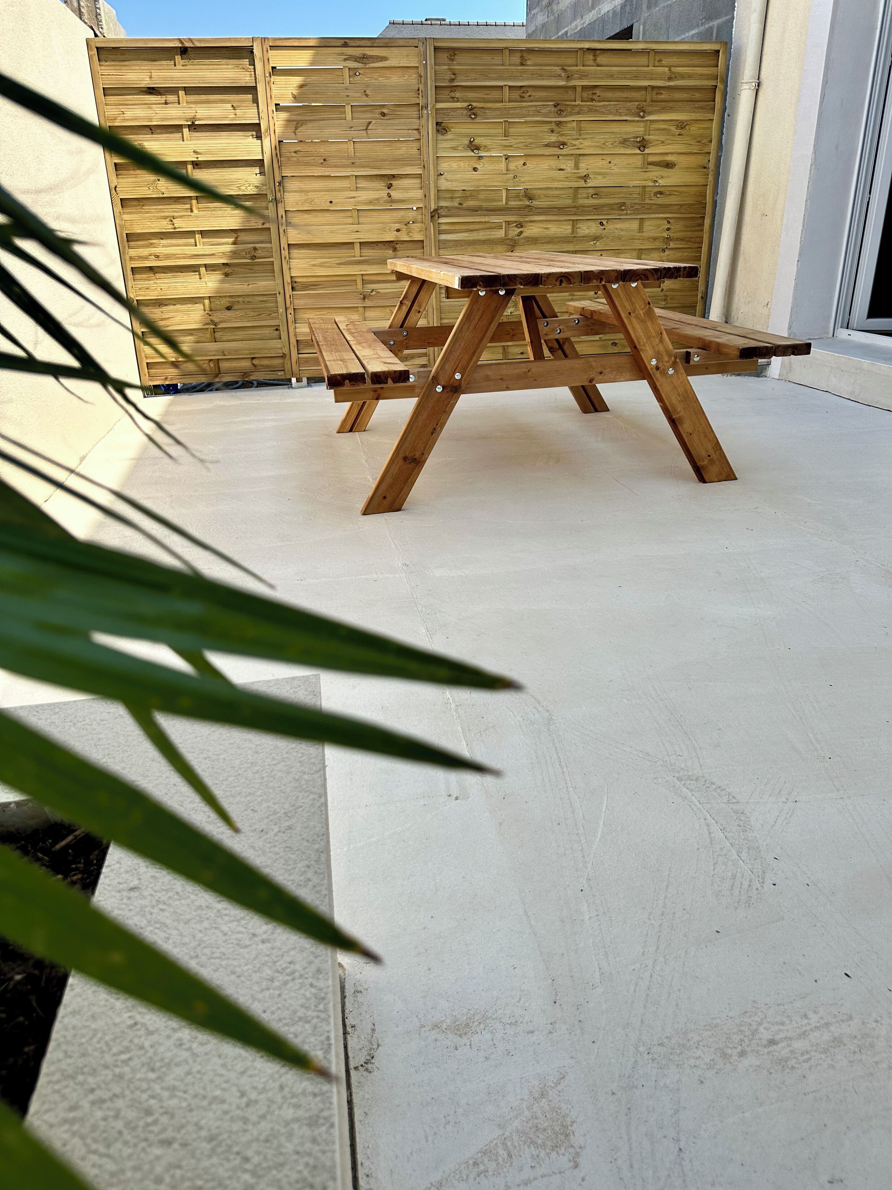 Uma mesa de piquenique de madeira em área externa coberta com piso de concreto.