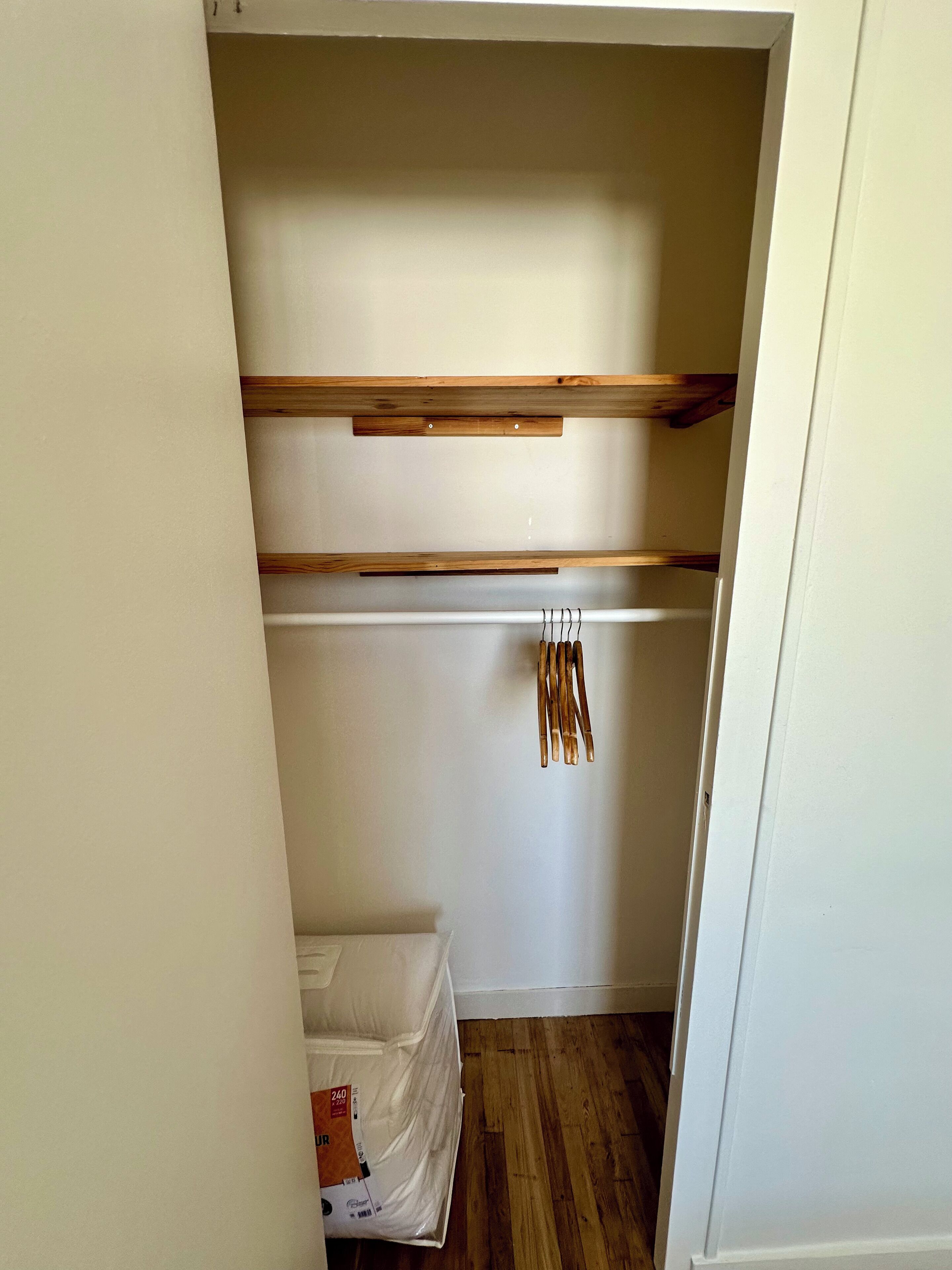 A small, narrow closet with wooden shelves and a hanging rod.