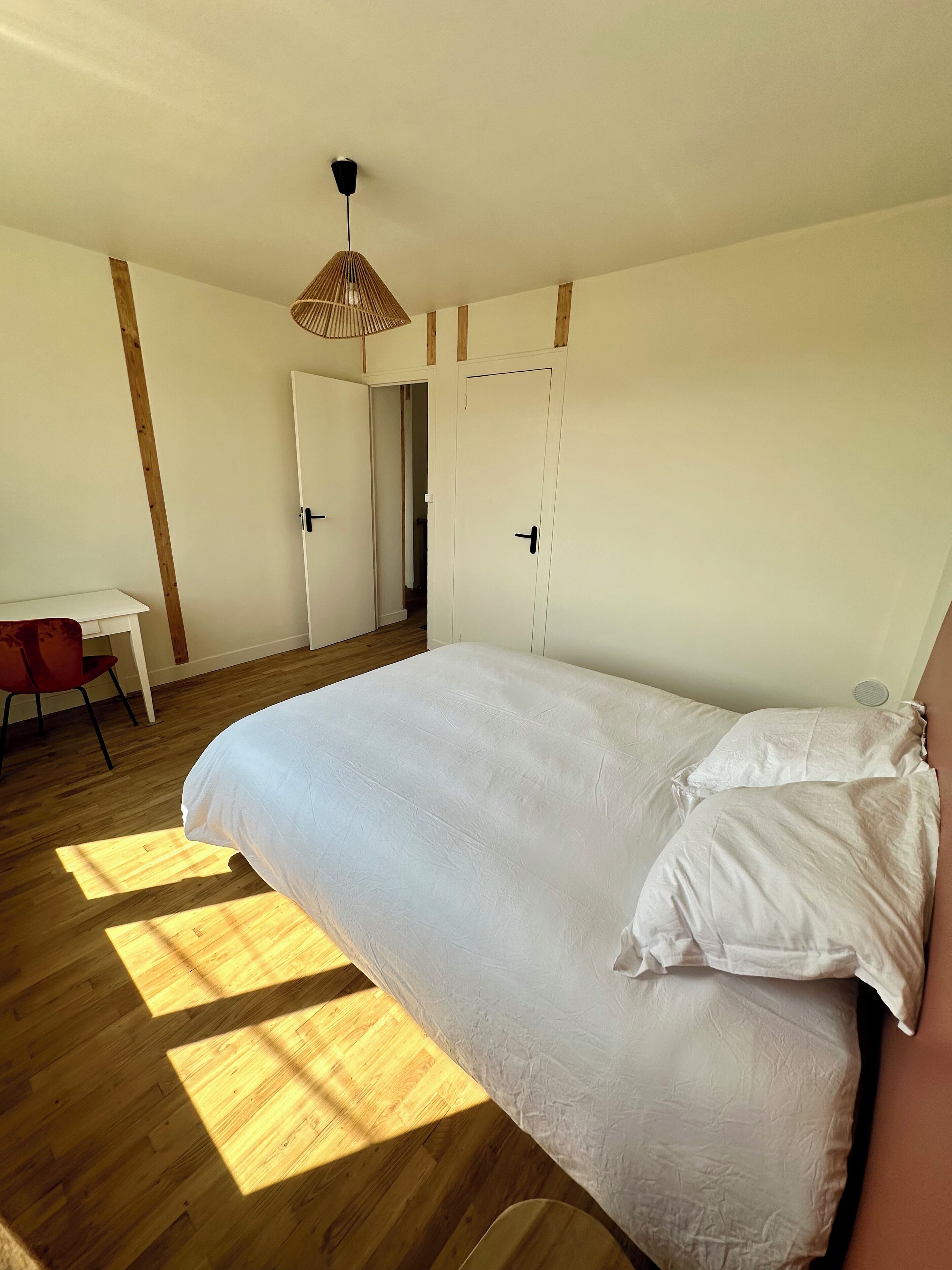 Un dormitorio con una cama grande, piso de madera, un escritorio y una silla.