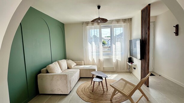 Ein Wohnzimmer mit einer Couch, einem Couchtisch, einem Fernseher und einem großen Fenster mit Vorhängen.