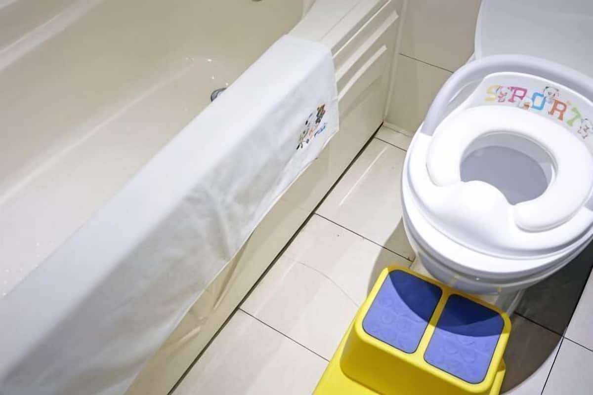 A bathroom with a bathtub, toilet, and a small yellow step stool.