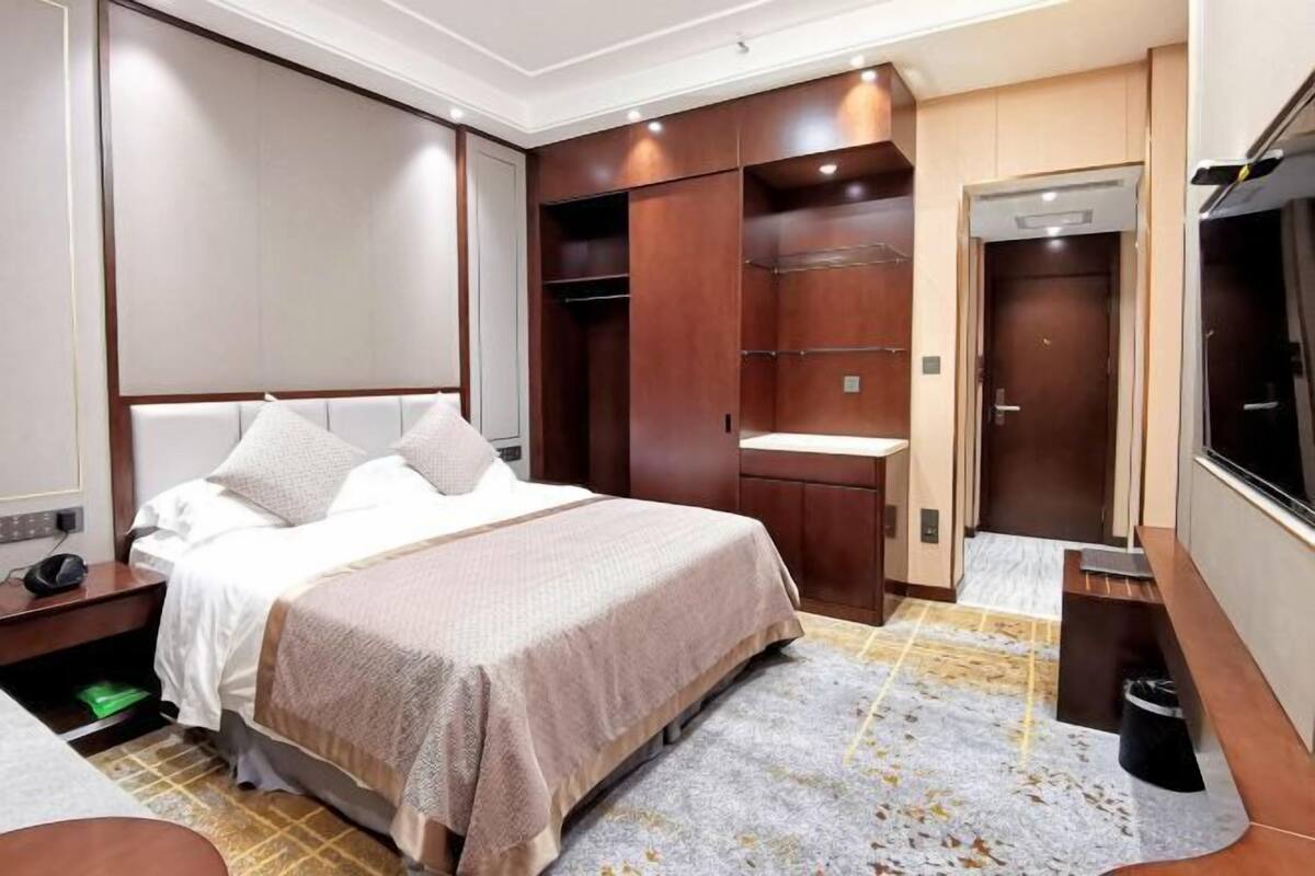 A hotel room with a bed, a desk, a wardrobe, and a television.