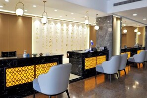 A hotel reception area with a black reception desk, white chairs, and a wall with illuminated calligraphy. - Yang Quan Hotel (Yangquan)