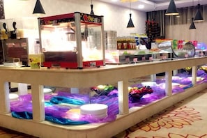 A buffet area with a self-service food station, a refrigerated display case, and a variety of food items. - Yang Quan Hotel (Yangquan)