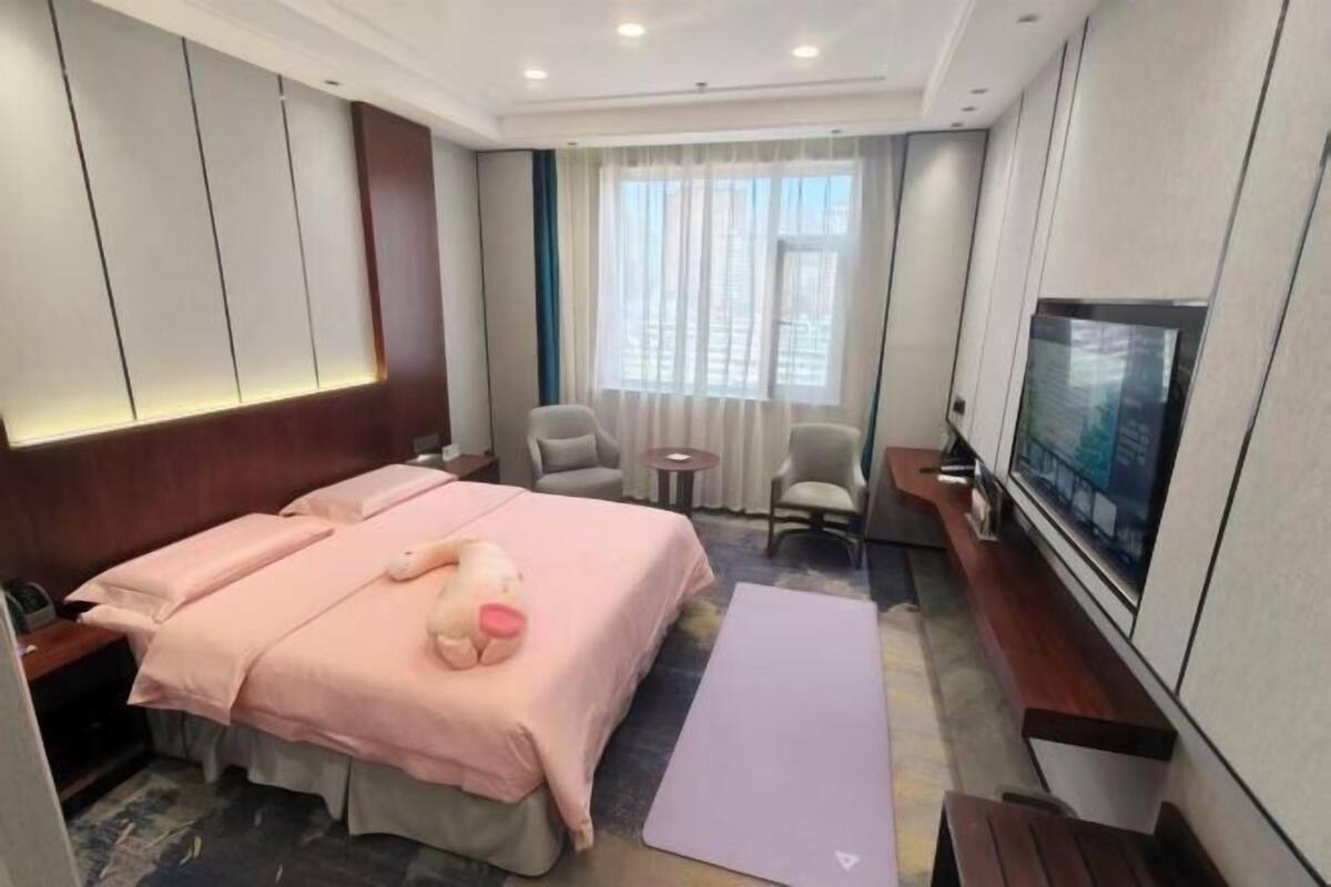 A hotel room with a bed, a TV, a desk, a chair, a small table, and a window.