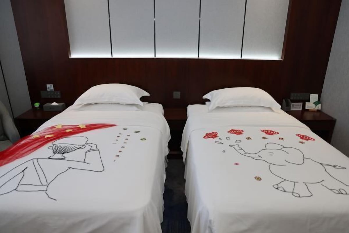 A hotel room with two beds, each with a white bedspread featuring a drawing.