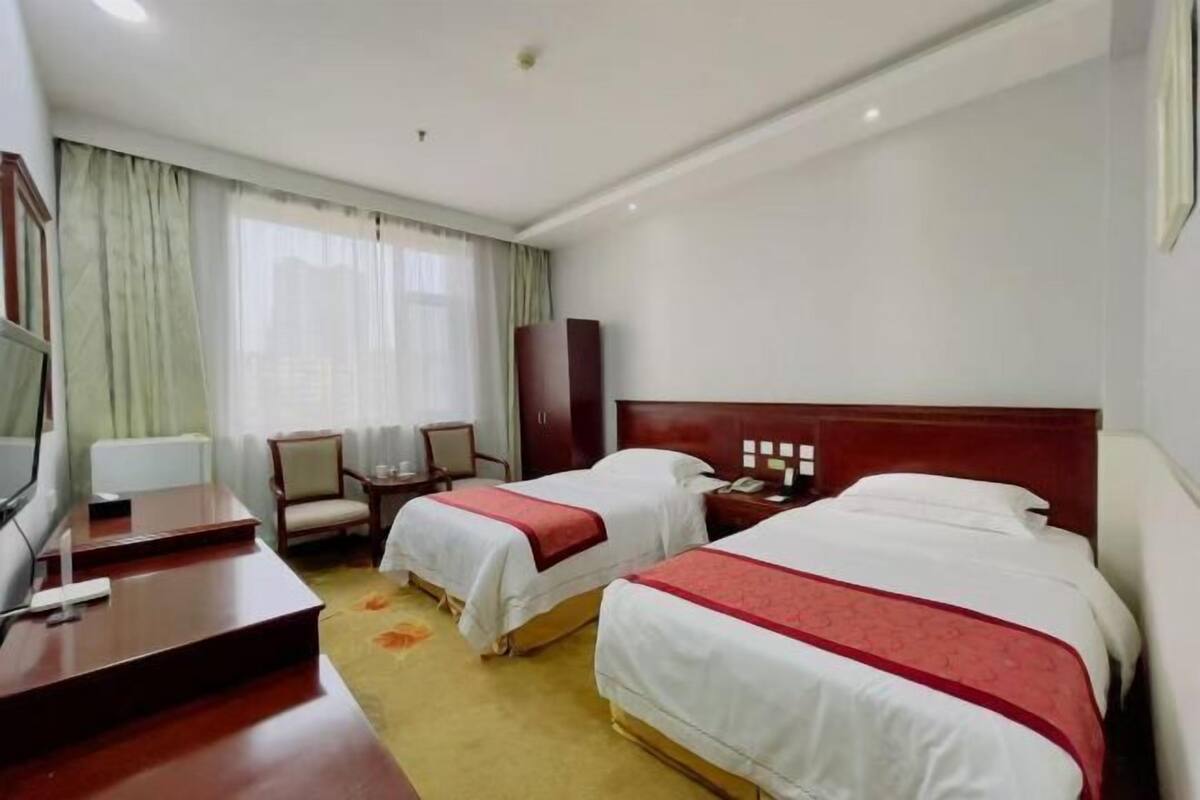 A hotel room with two beds, a desk, a chair, a TV, and a wardrobe.